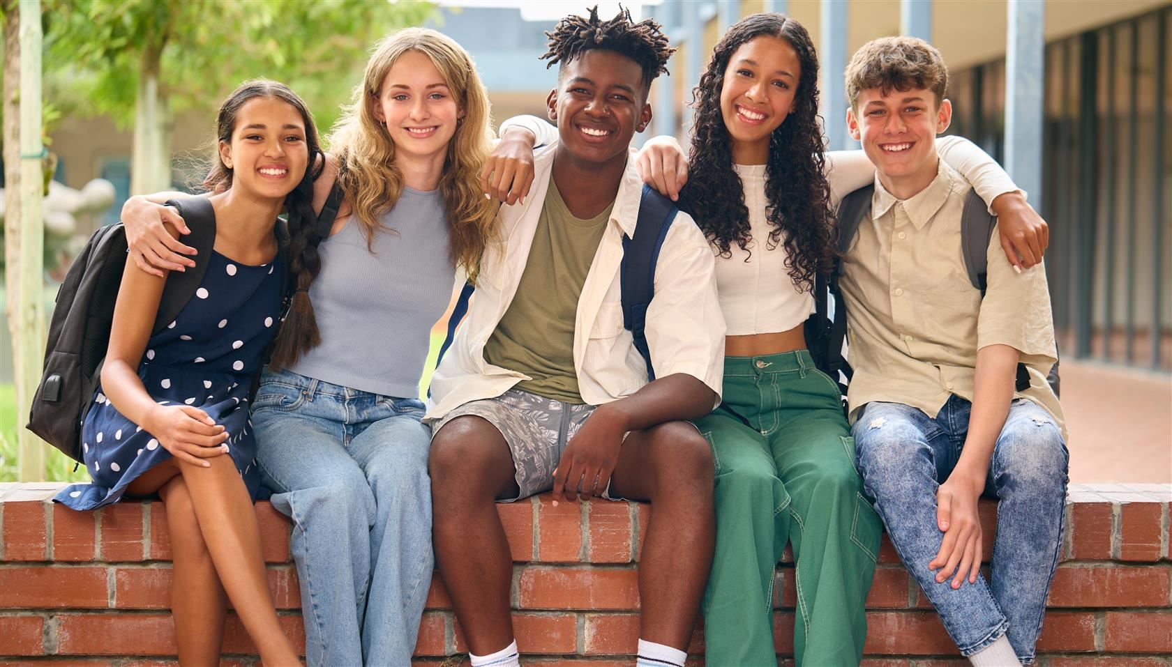 Happy group of teens sitting on a brick ledge.